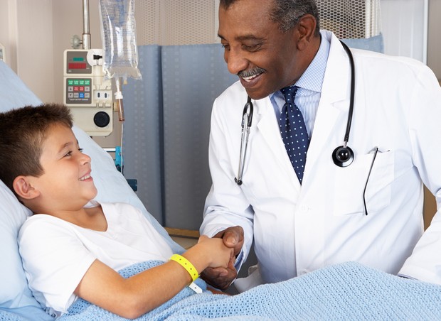 médico apertando a mão de criança sorrindo no leito após tratamento