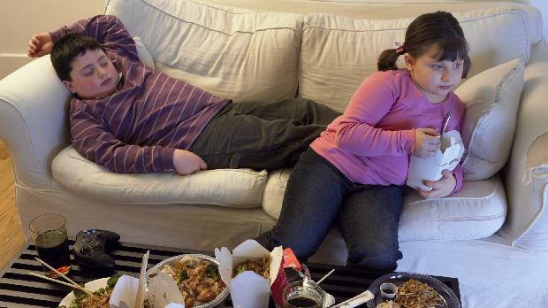 crianças sedentarias comendo besteiras no sofa